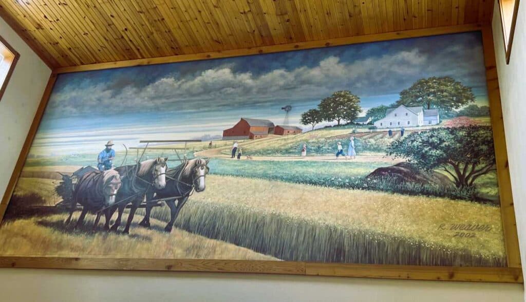 Rocky Weaver’s painting that depicts a local farmer harvesting wheat located at the Red Barn Shoppes in Shipshewana, IN