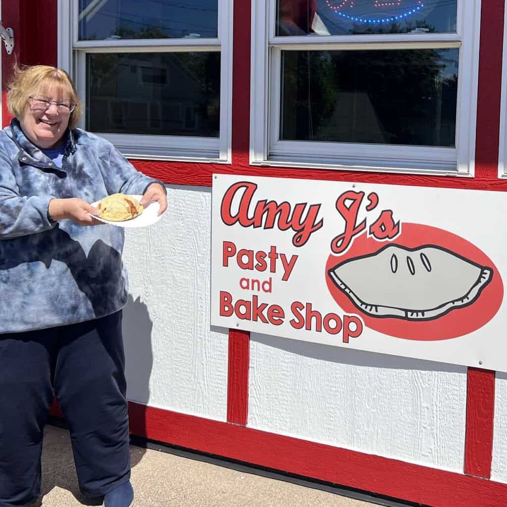 The author, Amy Piper with a pasty in front of Amy J''s Pasty and Bake Shop, eating a pasty is a Michigan Bucket List Item